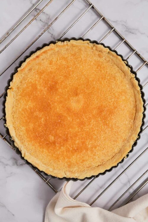Golden baked cheesecake in a black tart pan on a cooling rack.