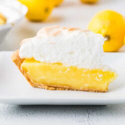Lemon meringue pie with a golden graham cracker crust and fluffy meringue topping on a white plate.