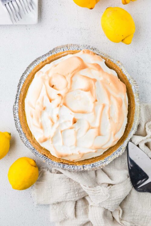 Lemon meringue pie with a golden crust topped with fluffy meringue and lemon drizzle on a white surface.
