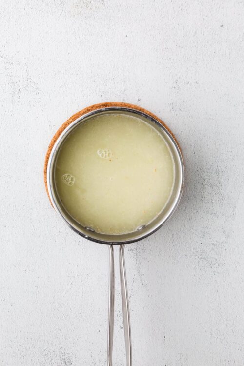 Creamy lemon curd in a stainless steel saucepan on a cork trivet, ready to spread or fill desserts.