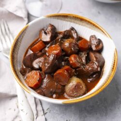 Slow cooker beef stew with carrots and onions in a white bowl.