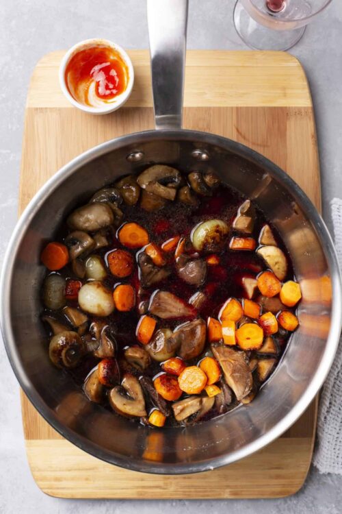 Mushroom and vegetable stew in a stainless steel pot on a wooden cutting board.