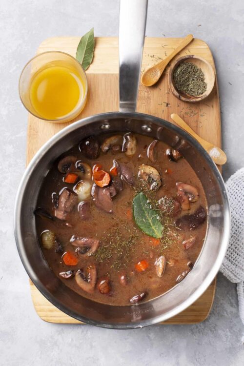 Savory mushroom and vegetable beef stew in a stainless steel pot with fresh herbs and spices.