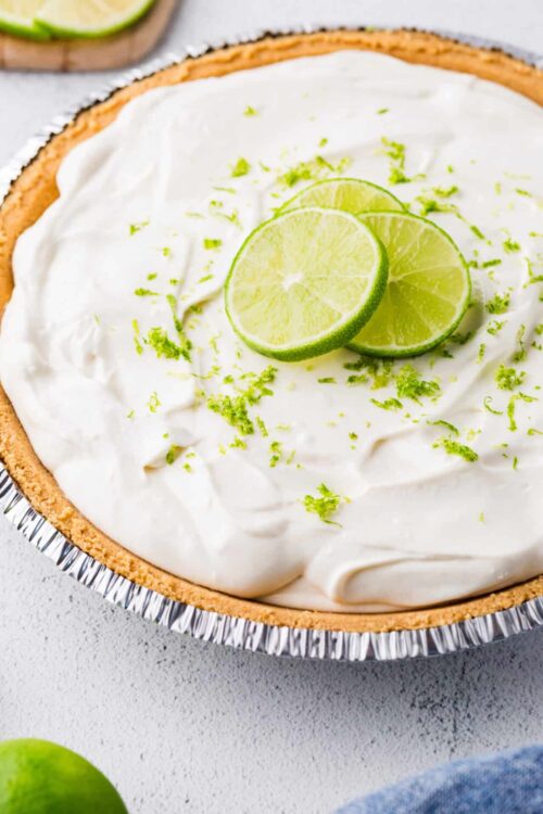 Lime pie with whipped cream and lime zest in a disposable pie dish.