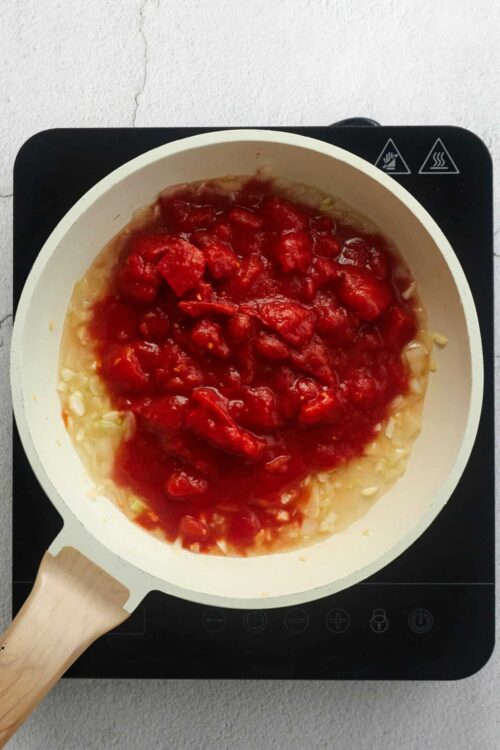 Rustic tomato sauce cooking in a white skillet on induction cooktop.