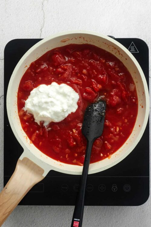 Creamy tomato sauce with dollops of sour cream and a black spatula stirrer in a white skillet.