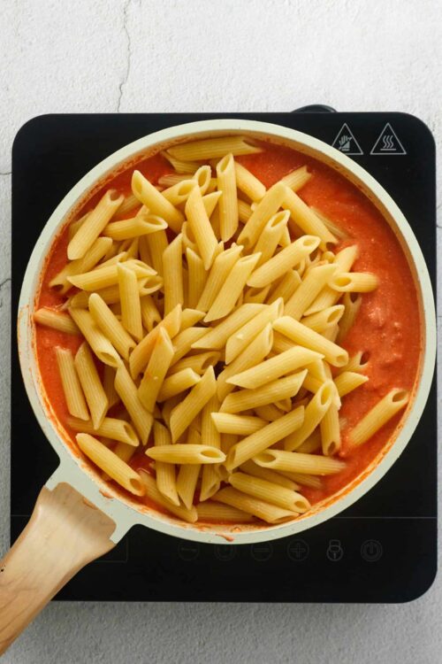 Pasta cooking in tomato sauce on induction cooktop.