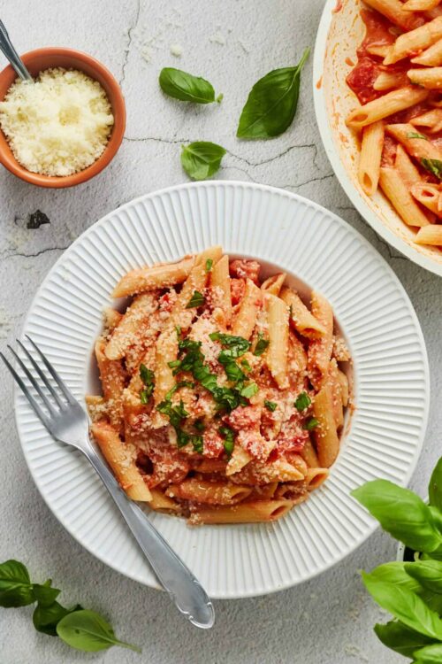 Pasta dish with tomato sauce, grated cheese, and basil on white plate.