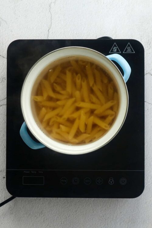 Boiling pasta in a pot on an induction cooktop, preparing a homemade pasta dish.