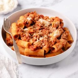 Creamy beef and tomato pasta with grated Parmesan cheese in a white bowl on marble surface.