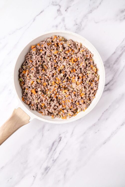 Ground beef and vegetable mixture in a white skillet on a marble surface.