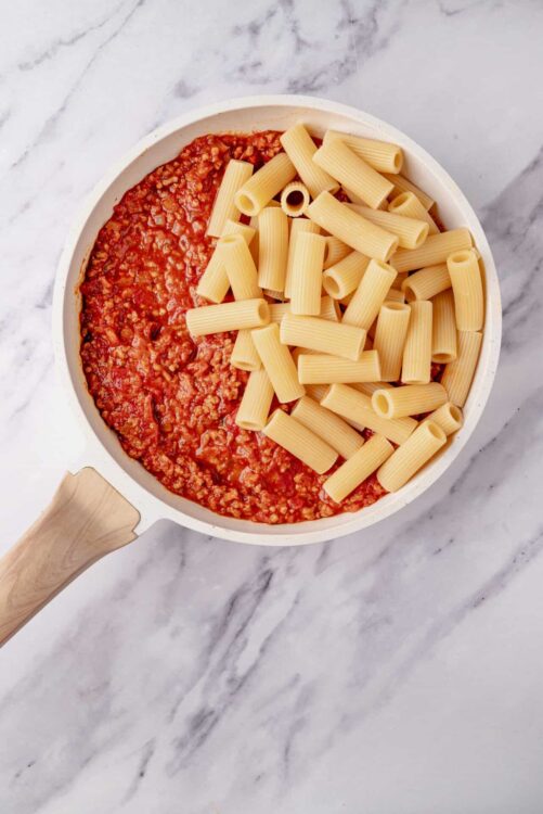 Cooked pasta with tomato meat sauce in a white skillet.