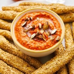 Creamy roasted red pepper hummus served with sesame seed breadsticks and almonds.