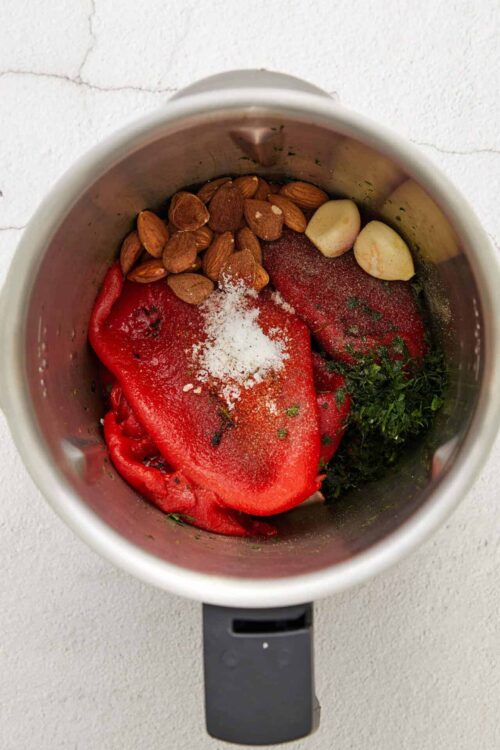Roasted red peppers, garlic, almonds, herbs, and spices in a blender for delicious homemade sauce.