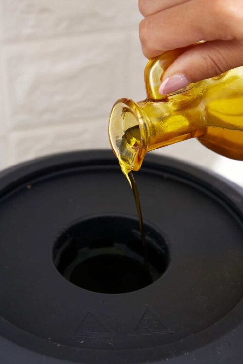 Golden olive oil being poured into a black air fryer basket.