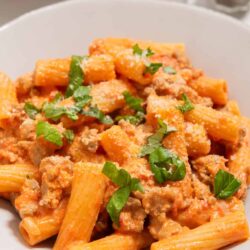 Creamy sausage and tomato pasta in a white bowl with fresh basil garnishes.