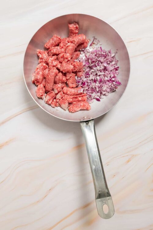 Minced raw meat and chopped red onions in a stainless steel skillet for cooking.