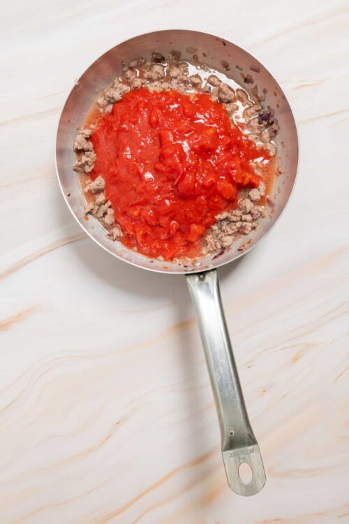 Cooked ground beef with tomato sauce in a skillet on a light marble surface.