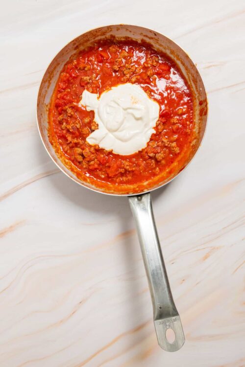 Savory meat sauce with creamy dollop of sour cream in a stainless steel skillet.