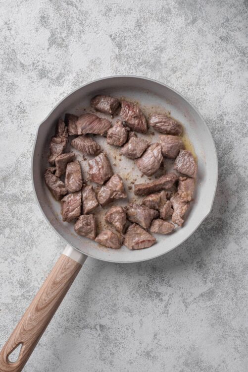 Cooked beef stew meat in a gray skillet on a textured gray surface.