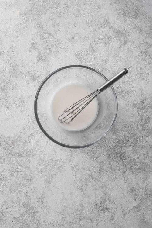 Cream in a glass bowl with a whisk for baking recipes.