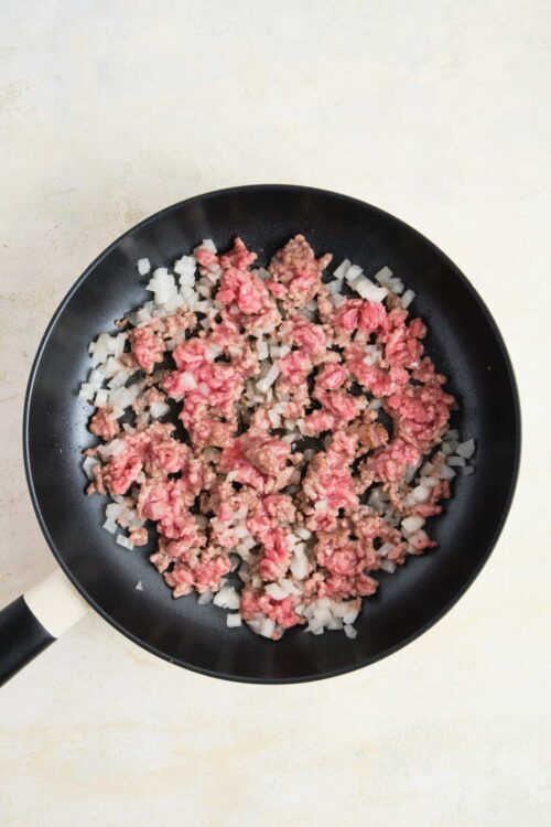 Minced onions and ground meat cooking in a black skillet, preparing for a recipe.