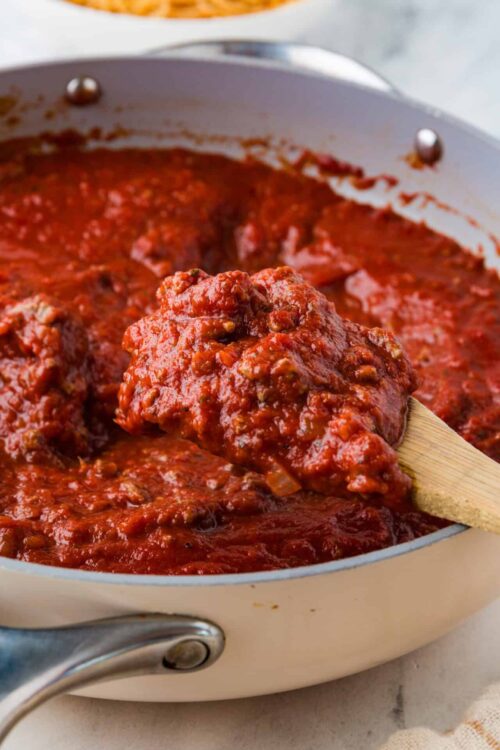 Creamy homemade marinara sauce in a white skillet with a wooden spoon.