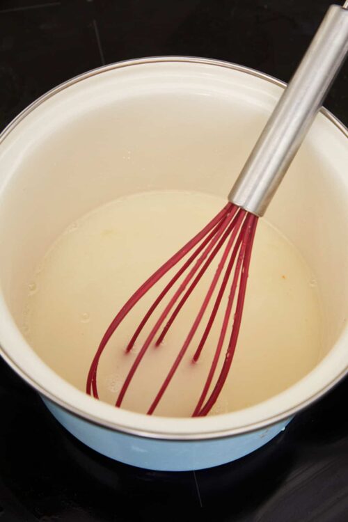 Creamy custard base with a red silicone whisk in a white saucepan, perfect for dessert recipes.