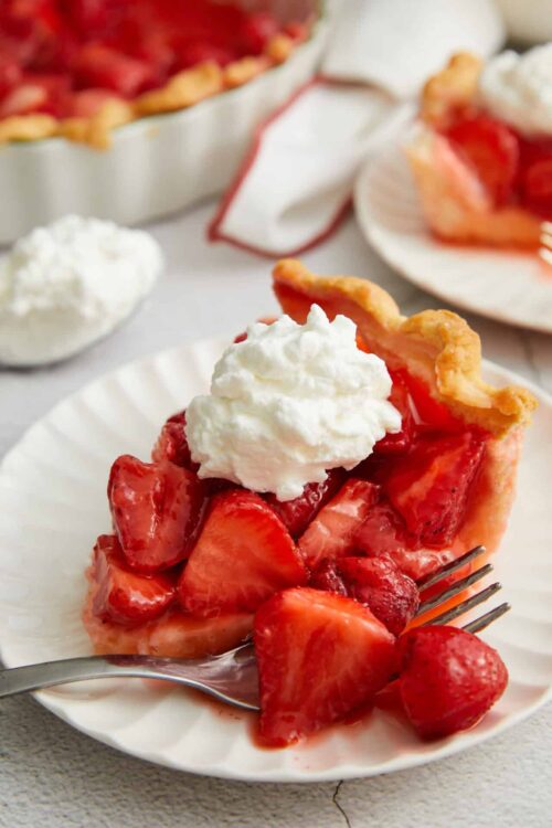 Fresh strawberry pie with whipped cream topping on a white plate.