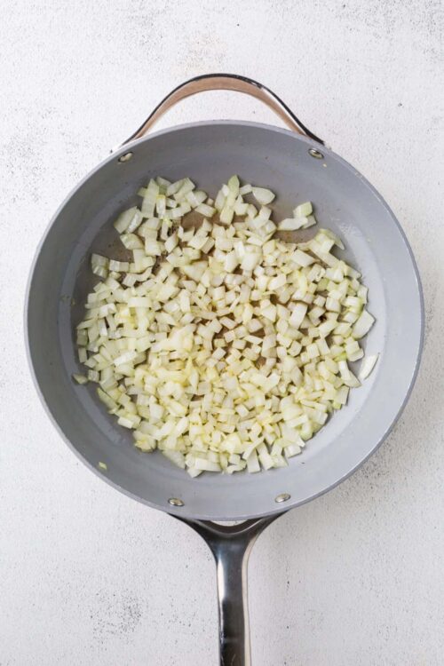 Diced onions sautéing in a gray skillet for cooking recipes.