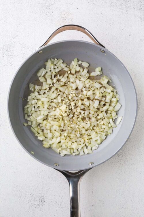 Diced onions and garlic sautéing in a stainless steel skillet for cooking.