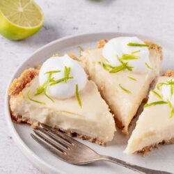 Lemon key lime pie with whipped cream and lime zest on a white plate.