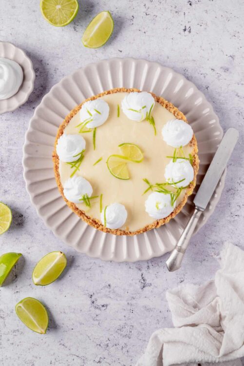 Lemon pie with whipped cream and lime garnish on a white plate.