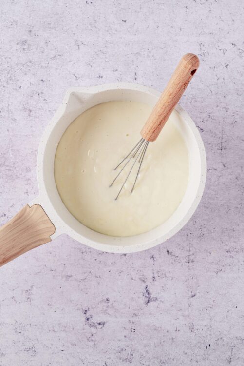 Creamy white sauce in a white mixing bowl with a whisk and wooden handle.