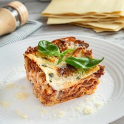 Creamy homemade lasagna with fresh basil on a white plate. Perfect comfort food dinner, layered with meat, cheese, and pasta.