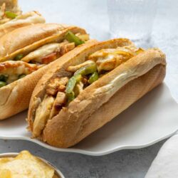Homemade chicken Philly cheesesteak sandwiches with melted cheese and sautéed green peppers on fresh hoagie rolls.