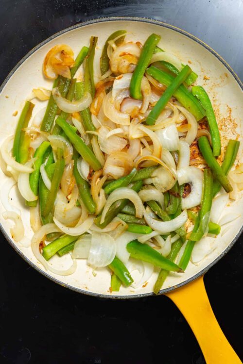 Sautéed green beans and onions in a yellow skillet on black stovetop.