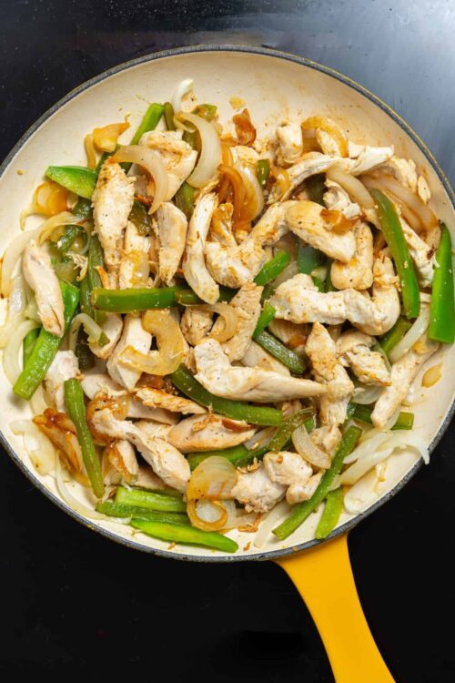 Sautéed chicken with green bell peppers and onions in a skillet.