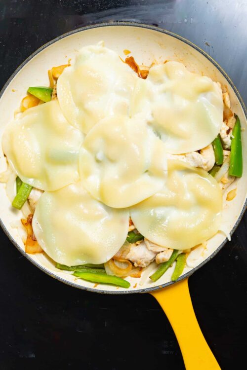 Cheesy chicken and green pepper skillet dish in a yellow frying pan.