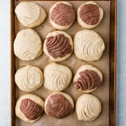 Buttery cookie dough balls topped with white and chocolate frosting, ready for baking.