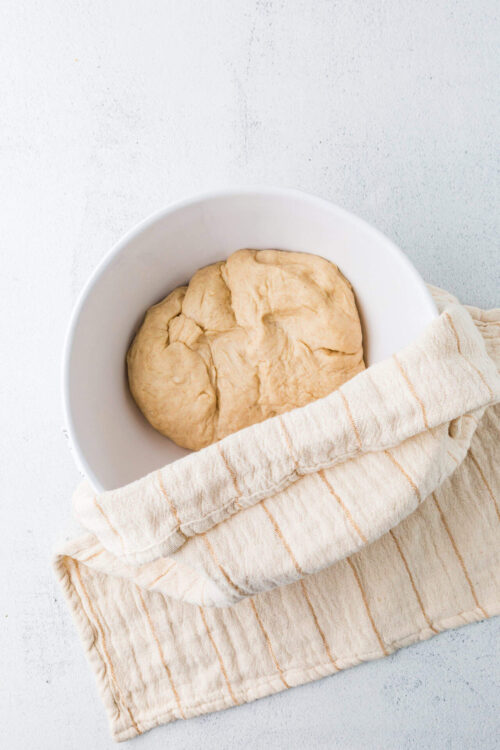 Soft rise pizza dough in a white bowl on a neutral background.