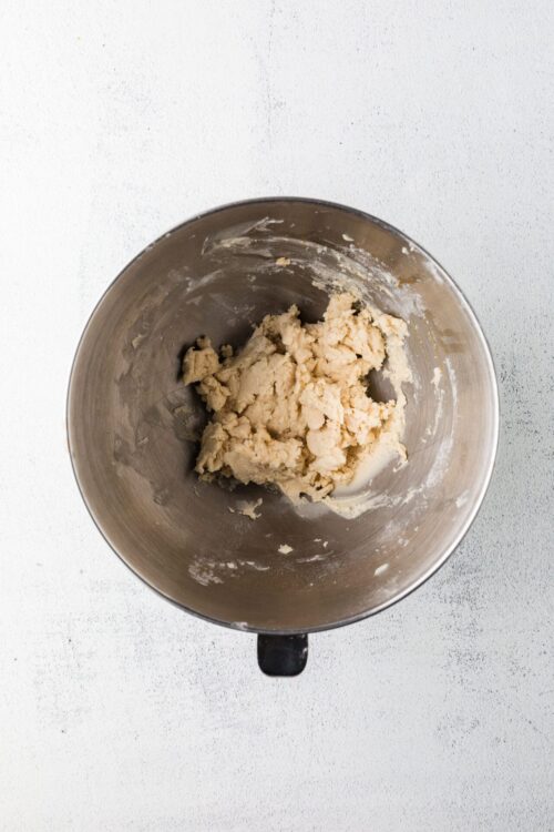 Crushed cookie dough in a mixing bowl on white surface for baking recipes.