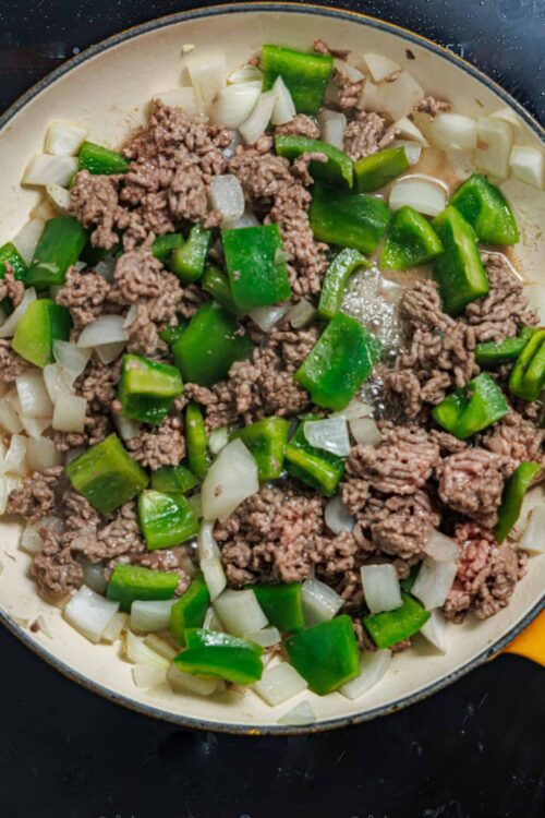 Sautéing ground beef, chopped onions, and green bell peppers in a skillet for a delicious savory dish.