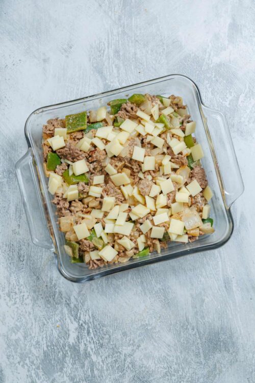 Softened ground beef casserole topped with melted cheese and green bell peppers in a glass baking dish.