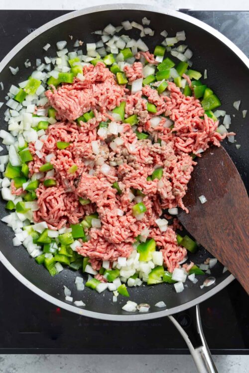 Ground beef, onions, and green peppers cooking in a skillet.