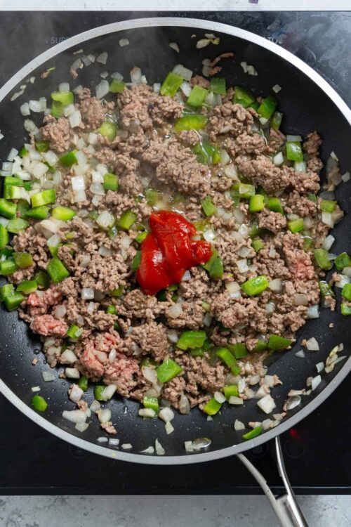 Sautéed ground beef with onions, green bell peppers, and tomato paste in a black skillet.