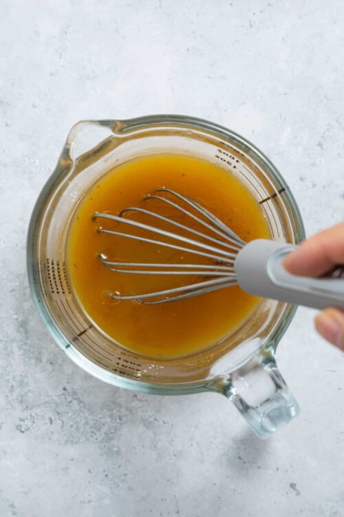 Smooth honey and vinegar mixture in a glass measuring cup with a whisk inside.