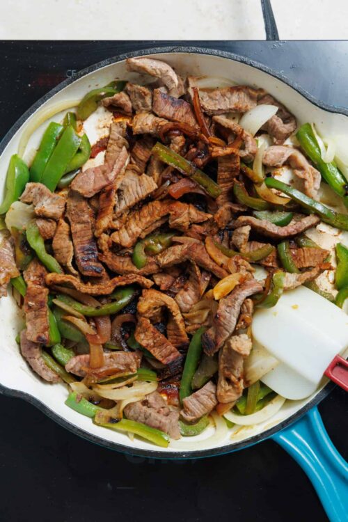 Sliced beef stir-fry with bell peppers and onions in a skillet.