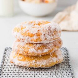 Buttery powdered sugar donuts on cooling rack with milk and bowl of strawberries in background.