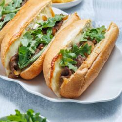 Fresh baked Italian subs with melted cheese, roasted beef, and fresh greens on a toasted hoagie bun.